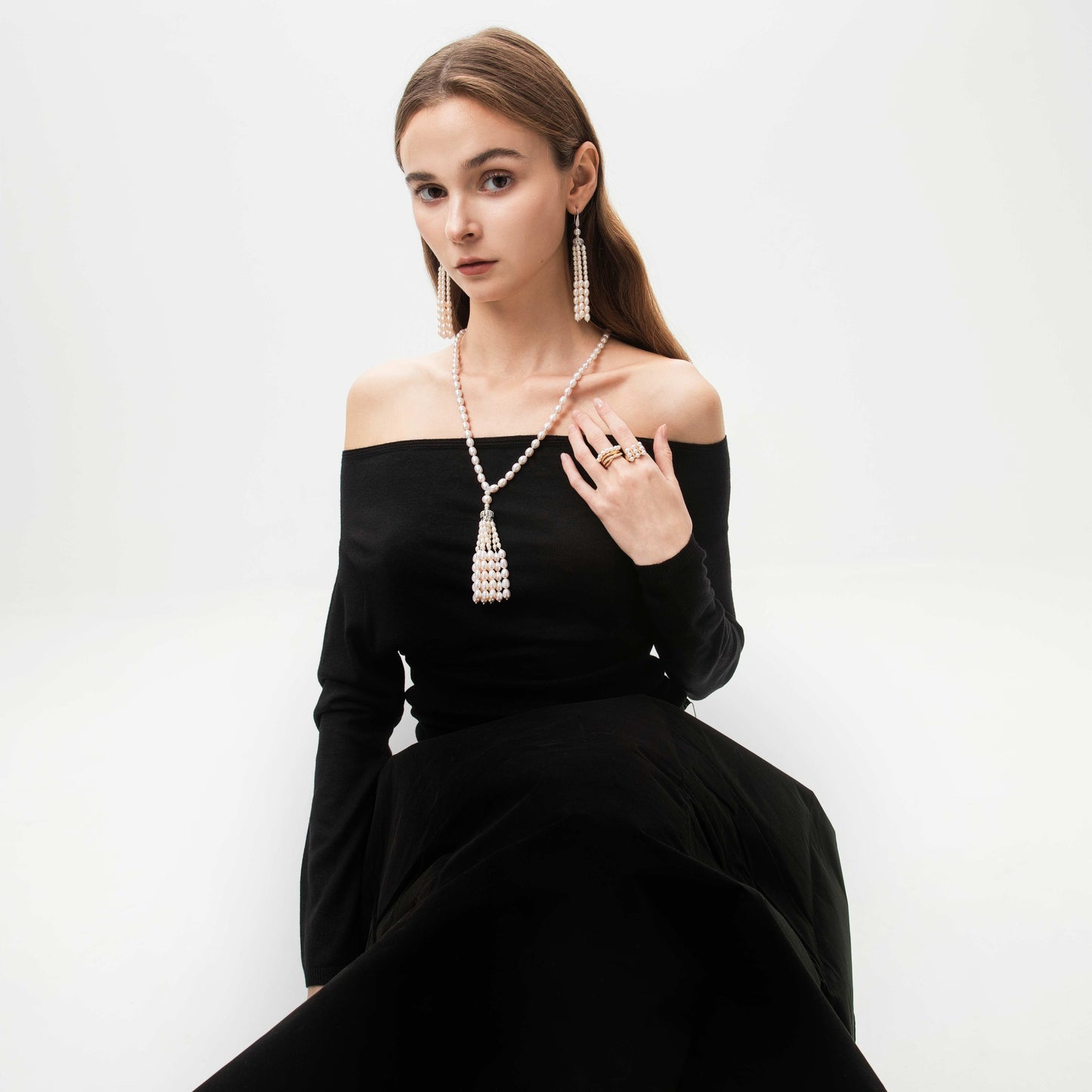 Woman wearing a black off-shoulder dress with pearl necklace and earrings set on a white background