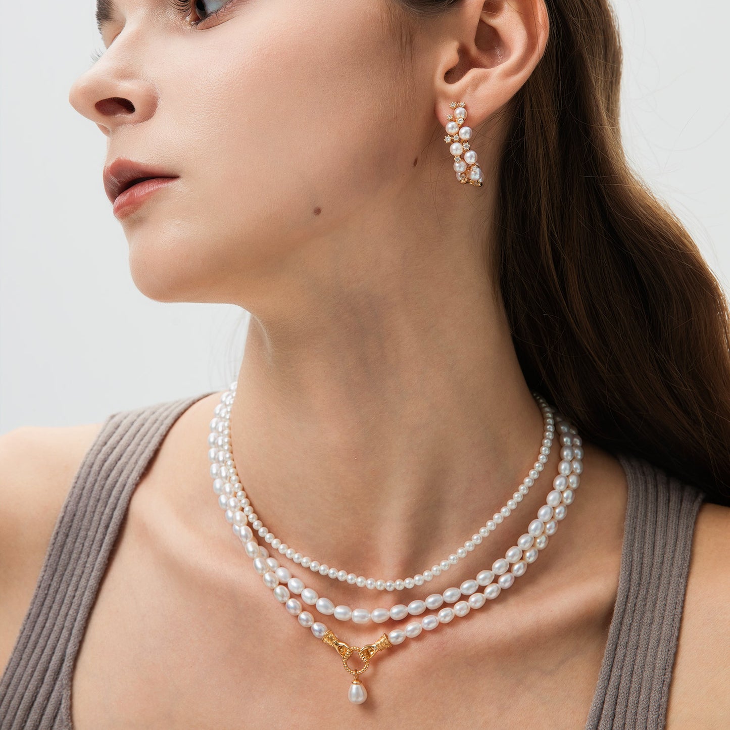 Close-up of a woman wearing pearl necklaces and earrings on a neutral background