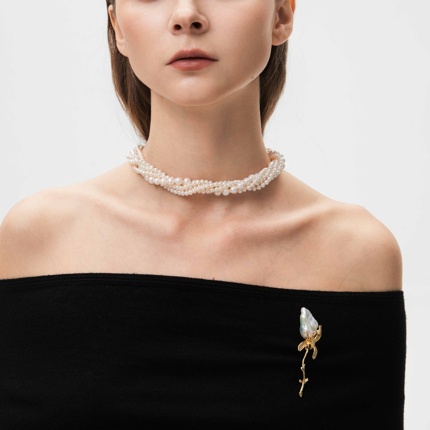 Woman wearing a pearl necklace with a matching brooch on a plain background