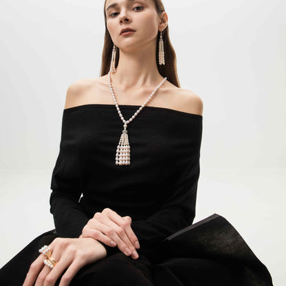 Woman wearing a black off-shoulder dress with a long pearl necklace and earrings on a white background