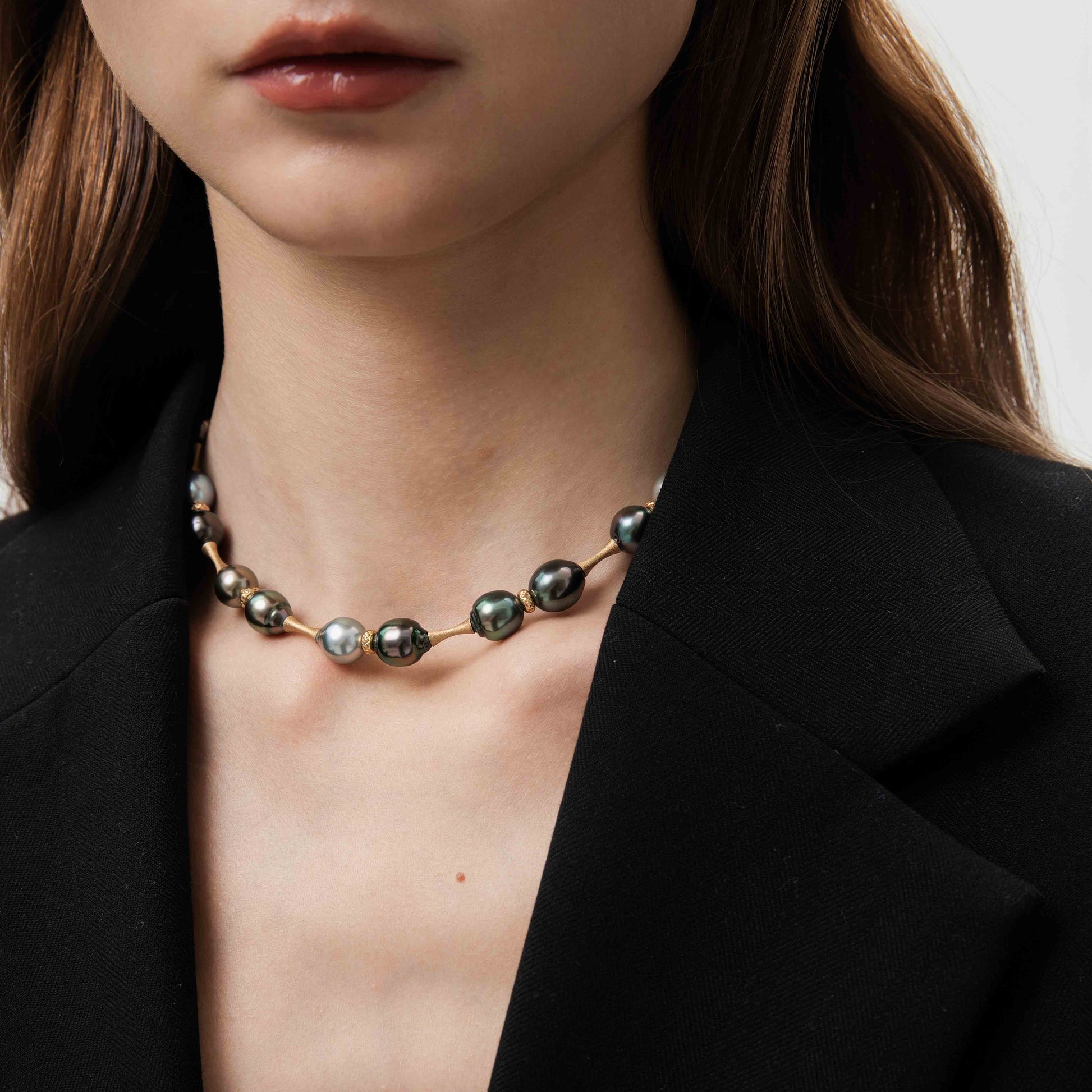 Necklace with beads worn by a person in a black blazer.