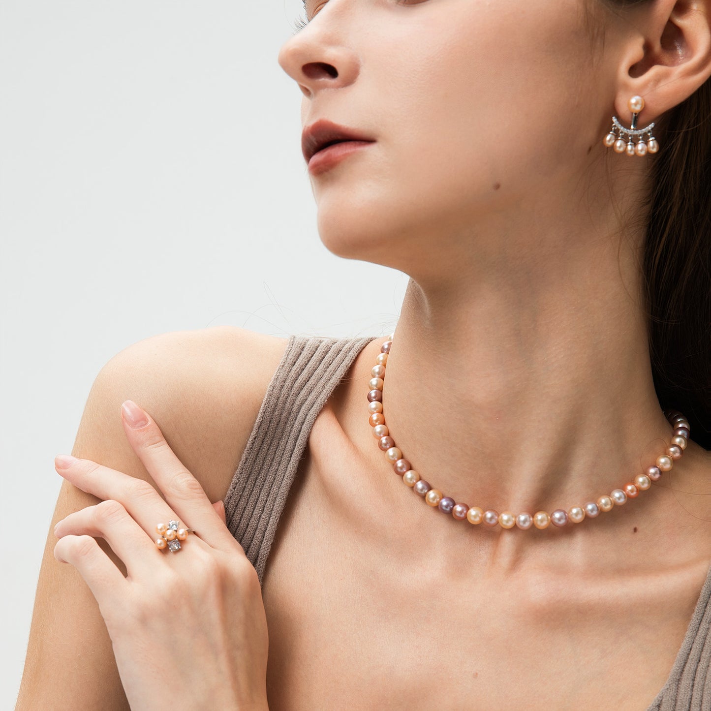 Woman wearing a pearl necklace, earrings, and ring on a light background