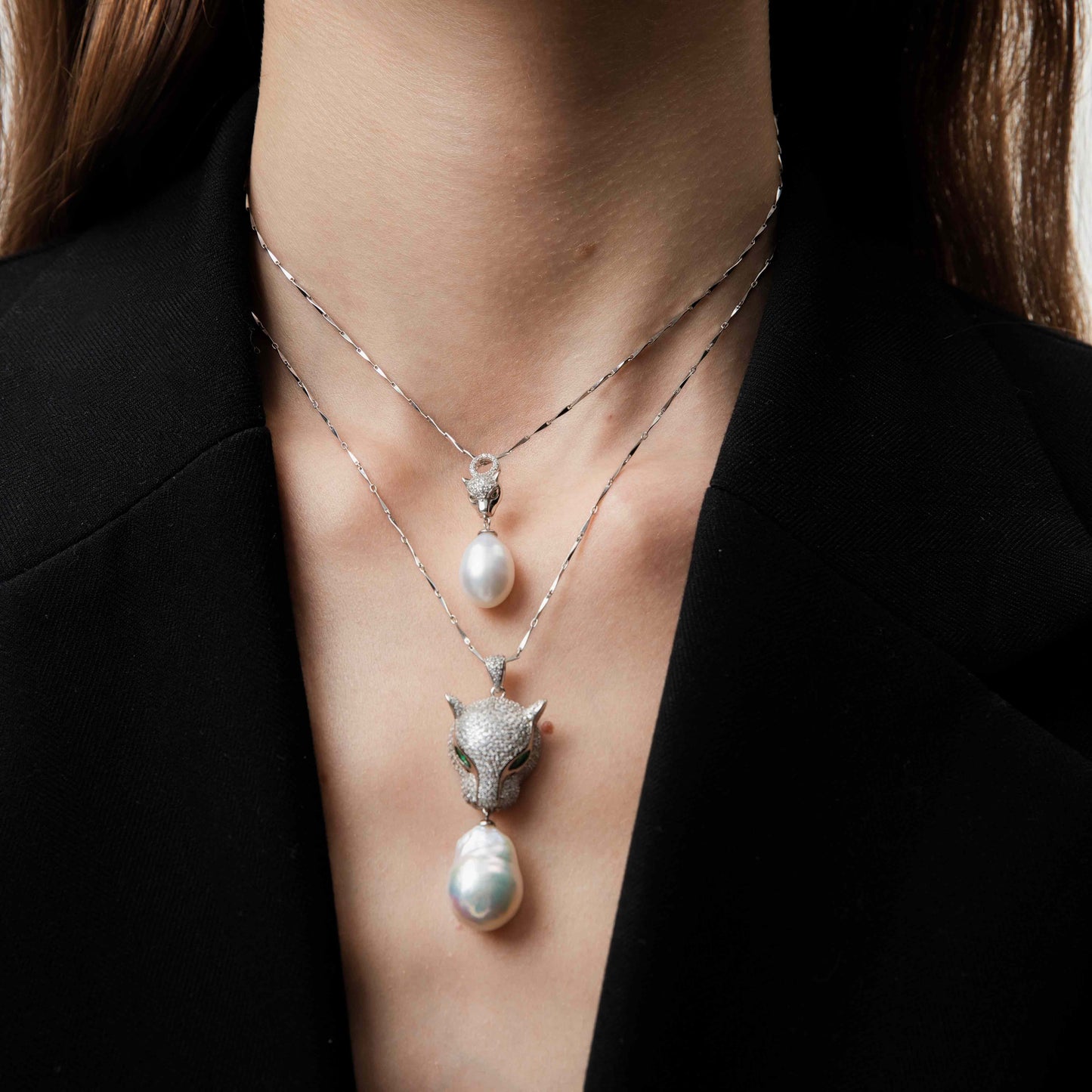 Two pearl necklaces with leopard pendants on a person wearing a black outfit.