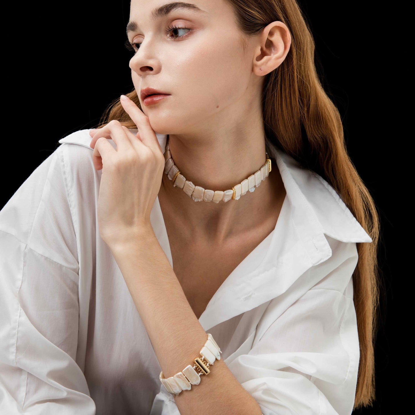 Woman wearing a white blouse, white bracelet and necklace with a black background