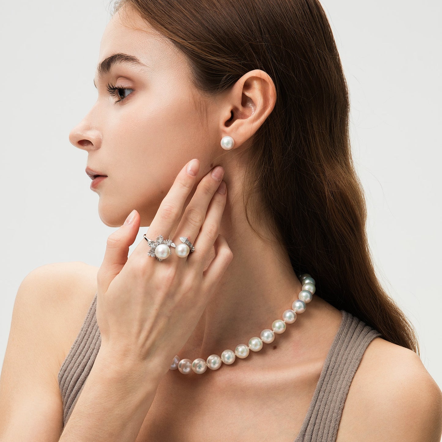 Woman wearing pearl jewelry including earrings, necklace, and ring on a light background