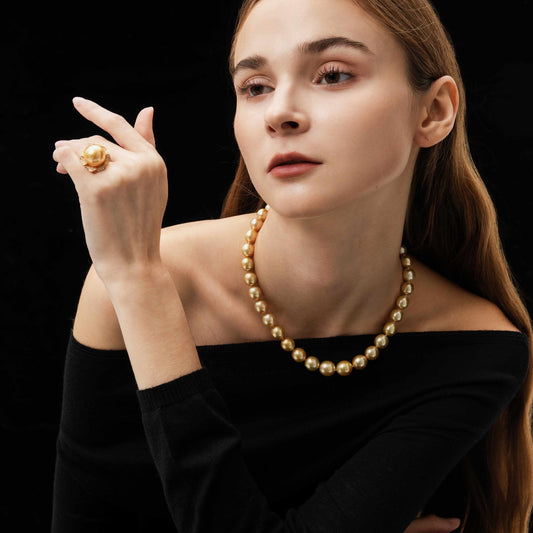 Woman wearing a gold necklace and ring against a black background
