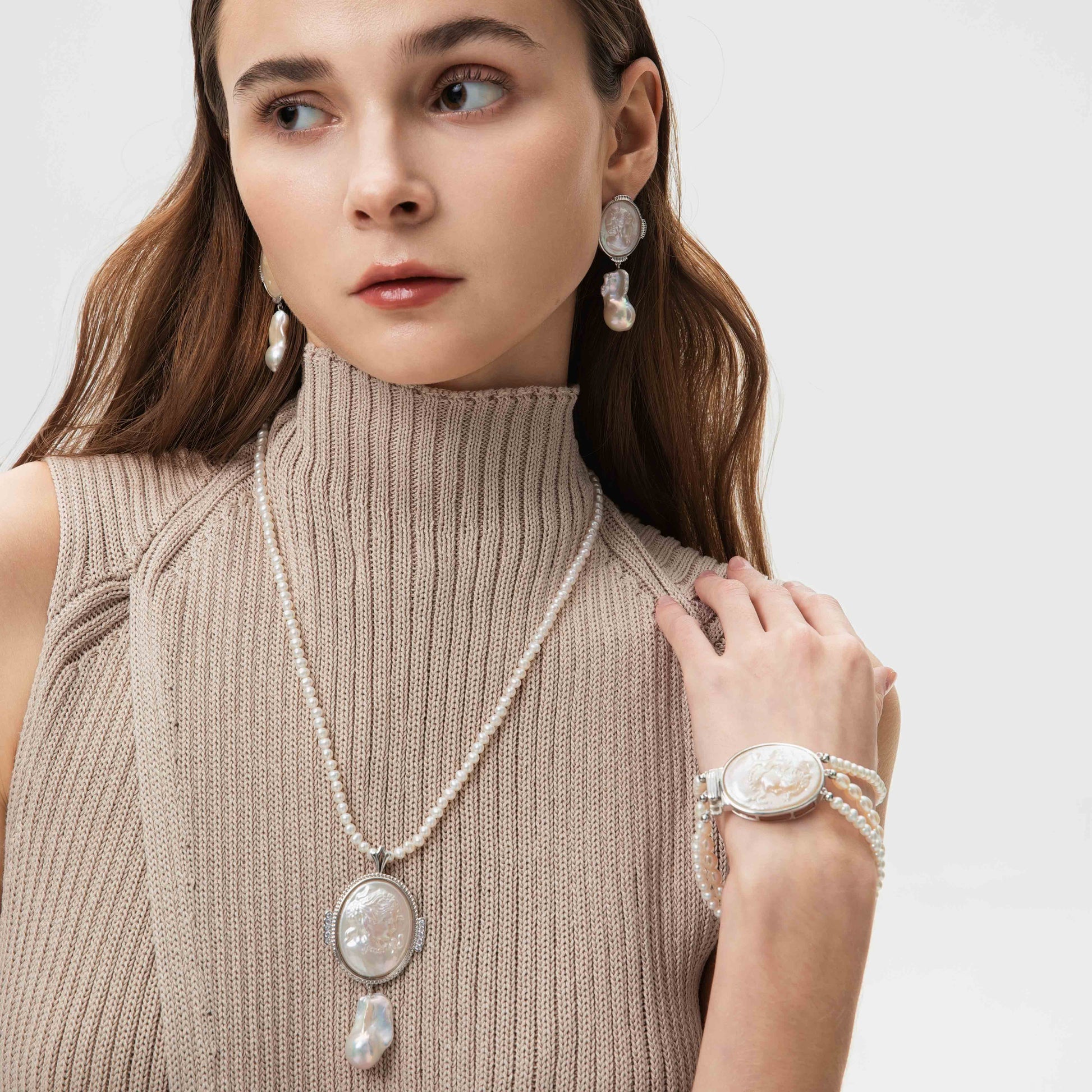 Woman wearing a pearl necklace, earrings, and bracelet against a white background