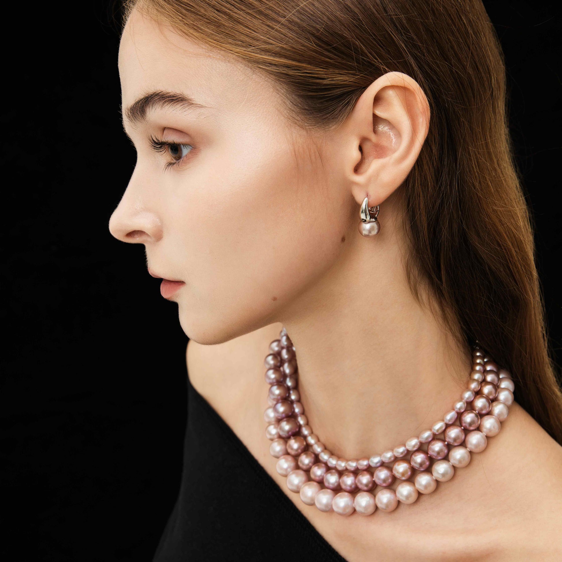 Woman wearing a Single Strand Graduated Pearl Necklace with Magnetic Gemstone Clasp and earrings on a black background
