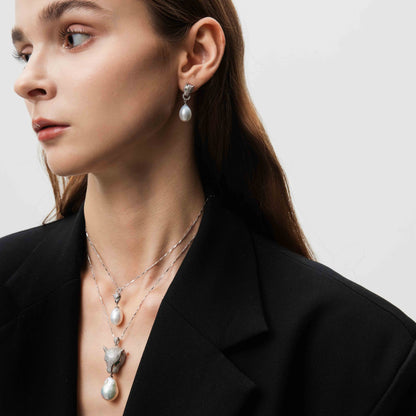 Woman wearing pearl earrings and necklaces against a neutral background