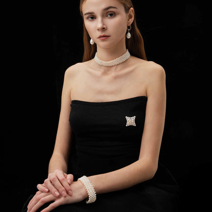 Woman wearing a black strapless dress with a pearl necklace, bracelet and earrings on a black background
