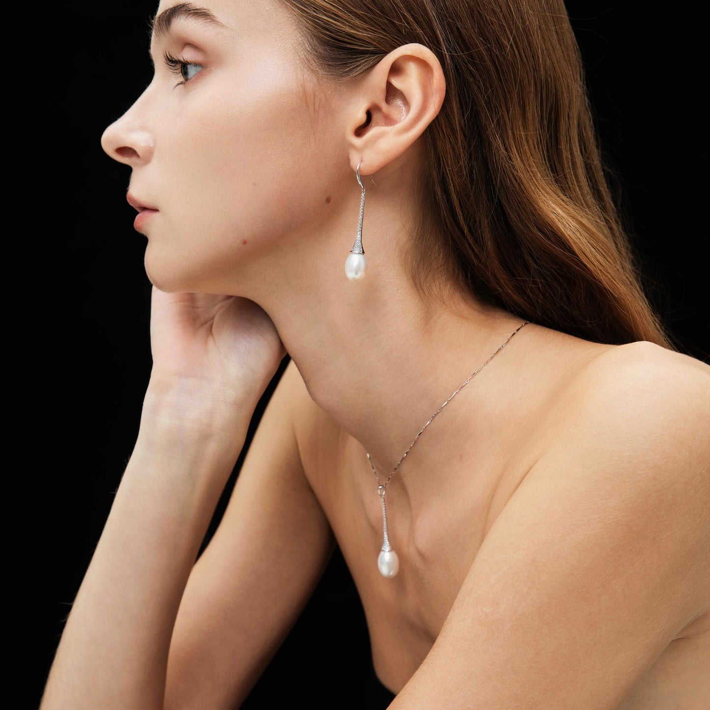Close-up of a woman wearing pearl earrings and necklace against a black background
